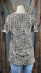 Celeste Clothing brand. Leopard print top with longer length and asymmetric cut out holes in beige trim on neck and sleeves.