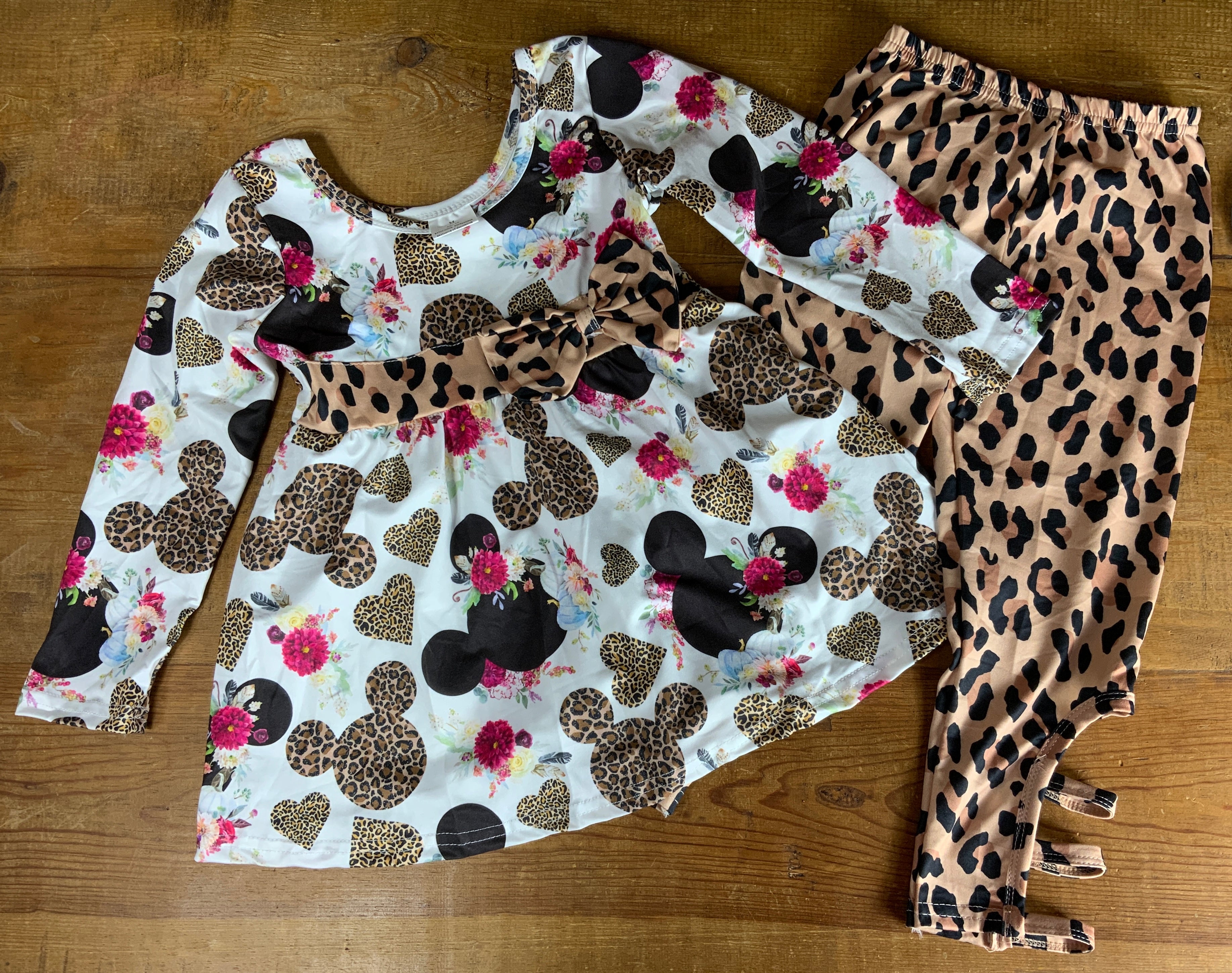 Yawoo Garments brand. Toddler. Top has leopard band and bow with black and leopard Mickey Mouse heads and pink flower accents. The elastic waist leggings have bottom leg cut outs and strap detail. Made from soft milk silk. Sizes 3T, 4T, 5-6T, 6-7T. $15